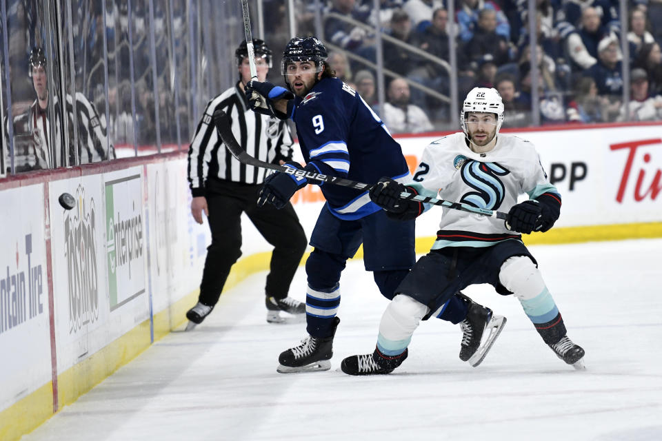 Seattle Kraken's Oliver Bjorkstrand (22) checks Winnipeg Jets' Alex Iafallo (9) as he dumps the puck into the Seattle zone during the second period of an NHL hockey game Tuesday, March 5, 2024, in Winnipeg, Manitoba. (Fred Greenslade/The Canadian Press via AP)