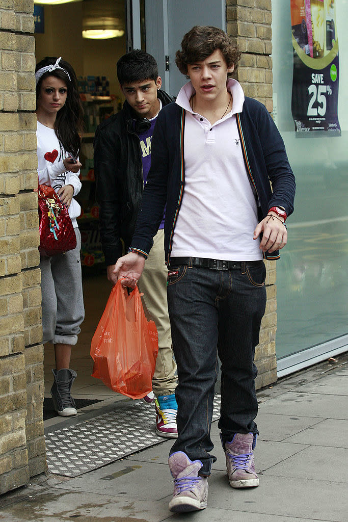 Harry on the street holding a shopping bag, with Cher and Zayn behind him leaving a store