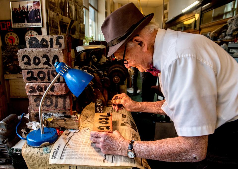 George Manias of George’s Shoeshine & Hatters paints a new brick for the new year Wednesday, Dec. 30, 2020, at his business in Downtown Peoria. The act is a Greek tradition intended to bring good luck. George has done this every year he’s been in business, amassing a collection of 75 bricks.