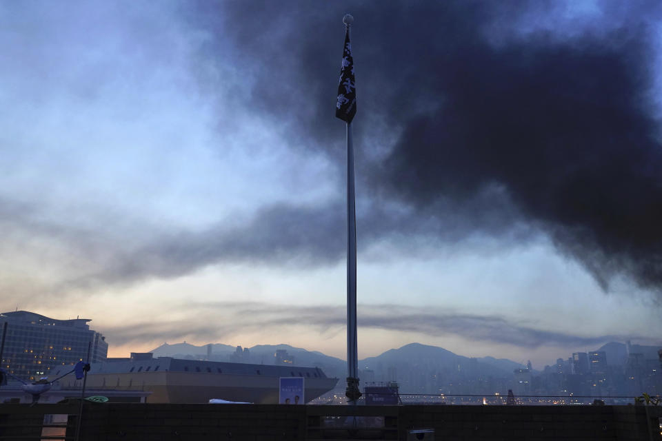 Smoke rises as a flag with the slogan "Liberate Hong Kong - Revolution of Our Times" hangs from a flagpole on the campus of Hong Kong Polytechnic University in Hong Kong, early Monday, Nov. 18, 2019. Police stormed into a Hong Kong university campus held by protesters early Monday after an all-night siege that included firing repeated barrages of tear gas and water cannons. (AP Photo/Vincent Yu)