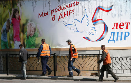 Men walk past a banner, which reads "We were born in DPR (Donetsk People's Republic)! DPR is five years old", in a street in the separatist-controlled city of Donetsk, Ukraine April 25, 2019. REUTERS/Alexander Ermochenko