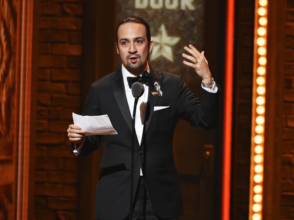 Lin-Manuel Miranda holds a piece of paper and speaks into a microphone