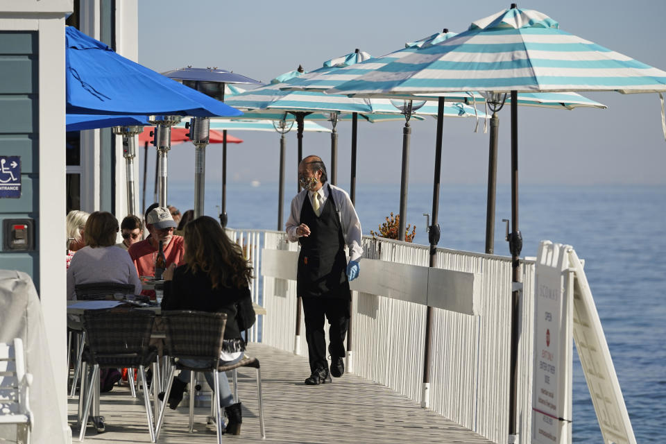 A waiter walks past tables of people dining outdoors at Scoma's restaurant, Friday, Dec. 4, 2020, in Sausalito, Calif. The health officers in six San Francisco Bay Area regions have issued a new stay-at-home order as the number of virus cases surge and hospitals fill. The changes announced Friday will take effect in most of the area at 10 p.m. Sunday and last through Jan. 4. It means restaurants will have to close to indoor and outdoor dining, bars and wineries must close along with hair and nail salons and playgrounds. (AP Photo/Eric Risberg)