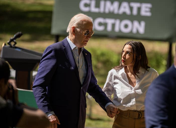 Joe Biden and Alexandria Ocasio-Cortez at a climate action event, with Biden in a suit and Ocasio-Cortez in a shirt and tan pants, holding hands