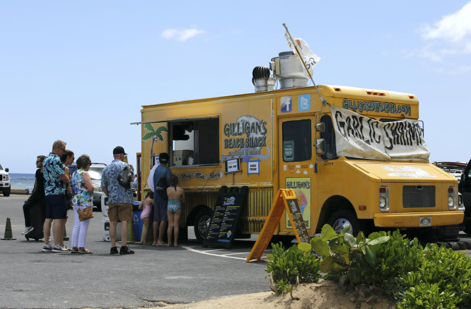 People line up at a food truck parked near Waikiki Beach in Honolulu, Monday, May 23, 2022. A COVID surge is under way that is starting to cause disruptions as schools wrap up for the year and Americans prepare for summer vacations. Case counts are as high as they've been since mid-February and those figures are likely a major undercount because of unreported home tests and asymptomatic infections. But the beaches beckoned and visitors have flocked to Hawaii, especially in recent months. (AP Photo/Caleb Jones)