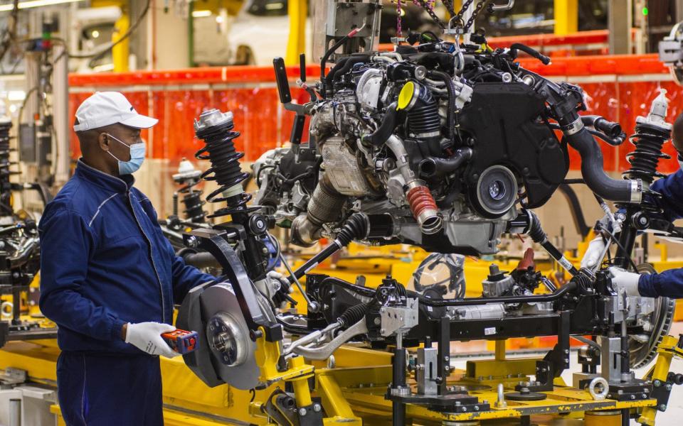 A worker wearing a protective face mask secures a suspension unit to an automobile chassis on the production line at the BMW South Africa , May 29, 2020.