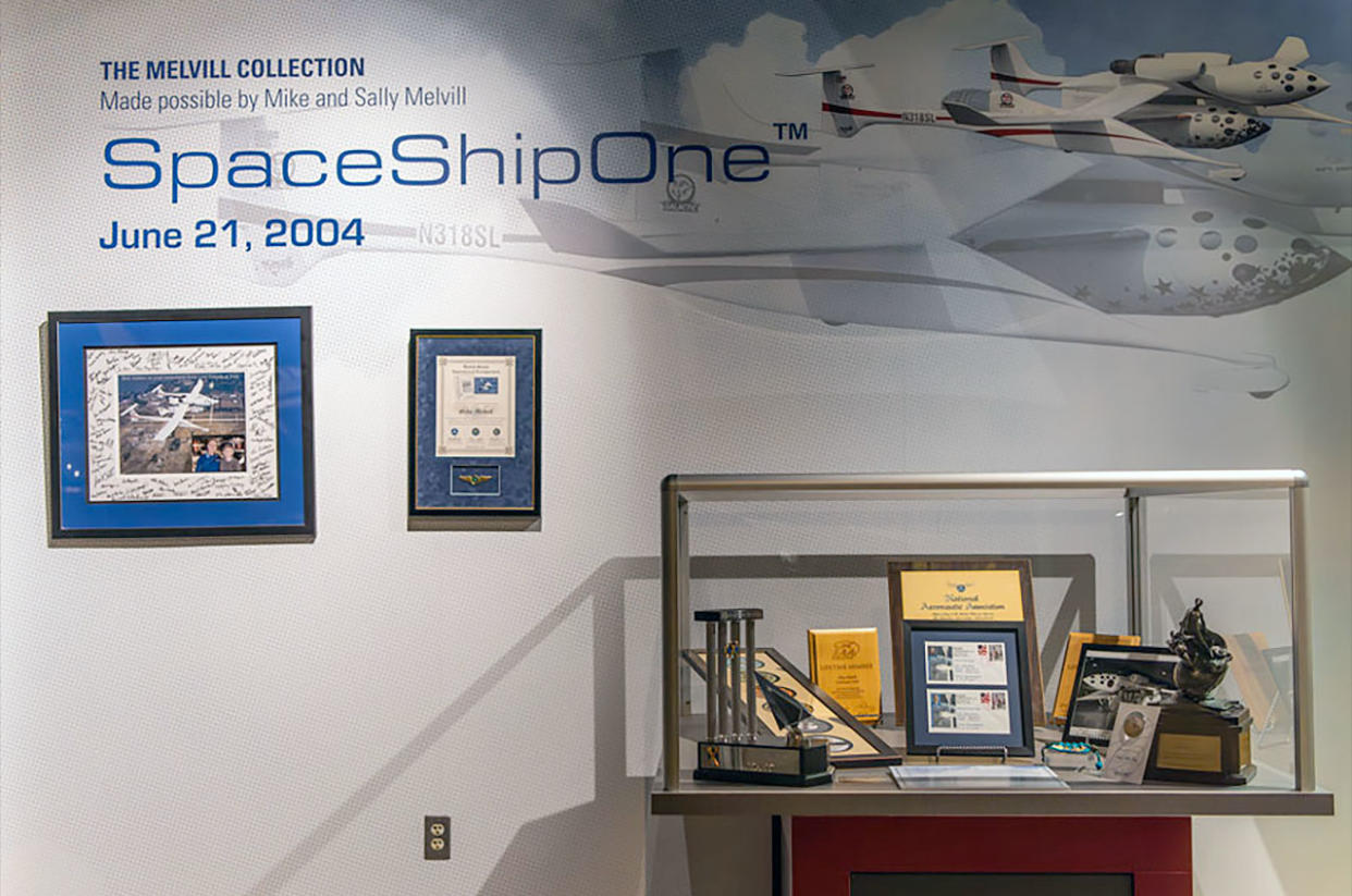  several plaques and other mementos on a white wall beneath the word "spaceshipone" 