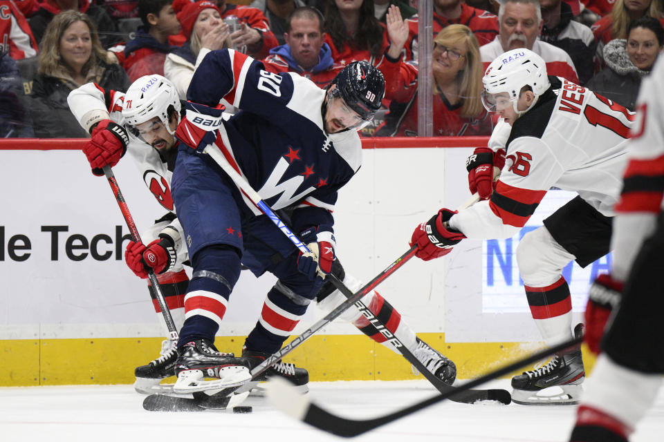 Washington Capitals left wing Marcus Johansson (90) battles for the puck against New Jersey Devils left wing Jimmy Vesey (16) and defenseman Jonas Siegenthaler (71) during the first period of an NHL hockey game, Saturday, March 26, 2022, in Washington. (AP Photo/Nick Wass)