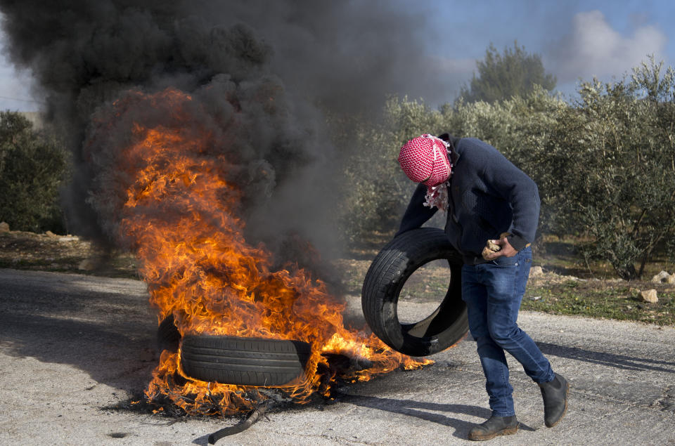 A masked Palestinian protester sets tires on fire during clashes with Israel forces as they protest Middle East peace plan announced Tuesday by US President Donald Trump, which strongly favors Israel, at Beit El checkpoint, near the West Bank city of Ramallah, Wednesday, Jan 29, 2020 (AP Photo/Majdi Mohammed)