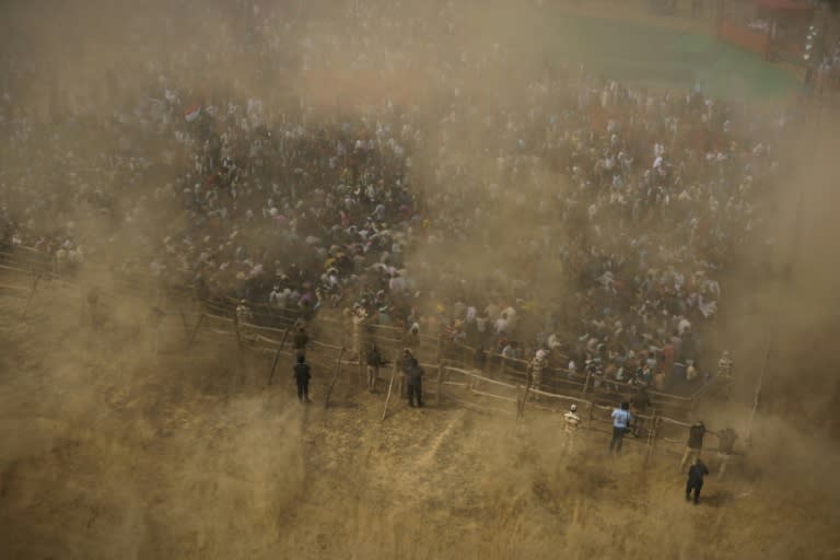 Supporters shield themselves from dust spread by a helicopter during a election rally in Bah, Uttar Pradesh