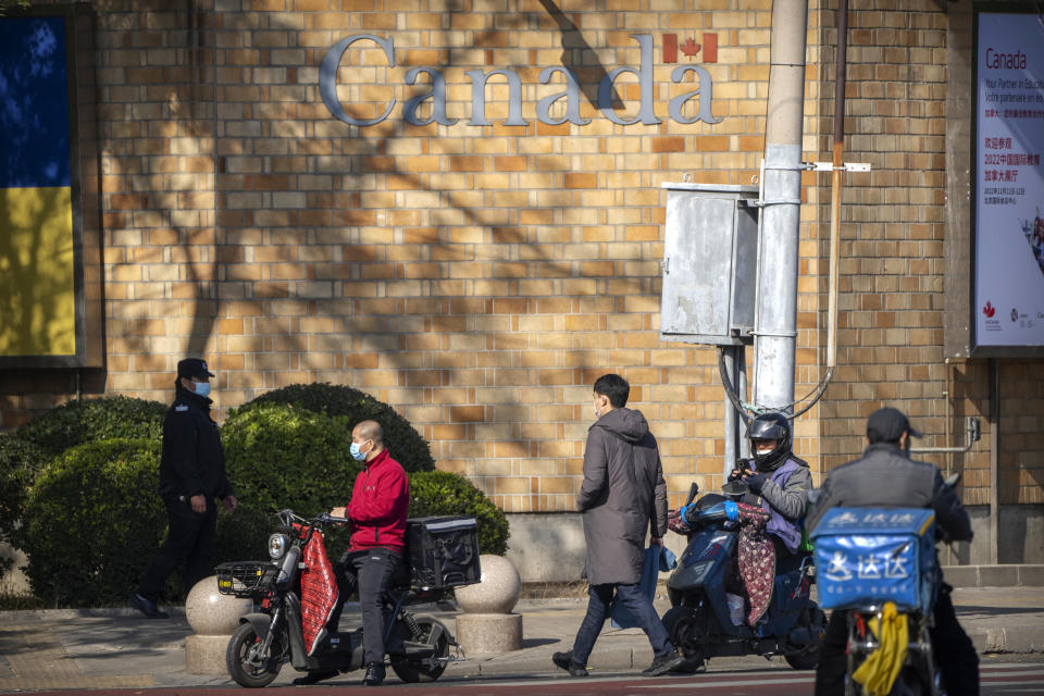 A security officer stands guard as people walk past the Canadian Embassy in Beijing, Thursday, Nov. 3, 2022. (AP Photo/Mark Schiefelbein)