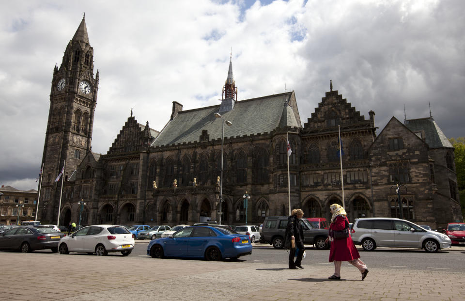 In this Wednesday, May 16, 2012 photo, pedestrians walk past town hall in Rochdale, England. The story of the abused Rochdale girls is tragic by any measure, but it has also become explosive. Because there is no getting around its racial subtext: The girls are white, and the men who used them for sex are Asian Muslims, mostly Pakistanis raised in Britain. Louis Kushnick, founder of the race relations resource center at the University of Manchester, said it has become convenient for white residents - including those beyond the far-right movement - to blame Muslims for the sex crimes. That view overlooks all the problems that left the girls vulnerable in the first place, he says, citing a deficient school system and a government-backed child care regime riddled with neglect and abuse. And he says the prolonged economic downturn has intensified resentments, with whites and Asians competing for the same "crap" jobs. "Blaming the Muslims lets us avoid addressing these questions,” he says. "Once we blame 'The Other,' we think we have an explanation that makes sense." (AP Photo/Jon Super)