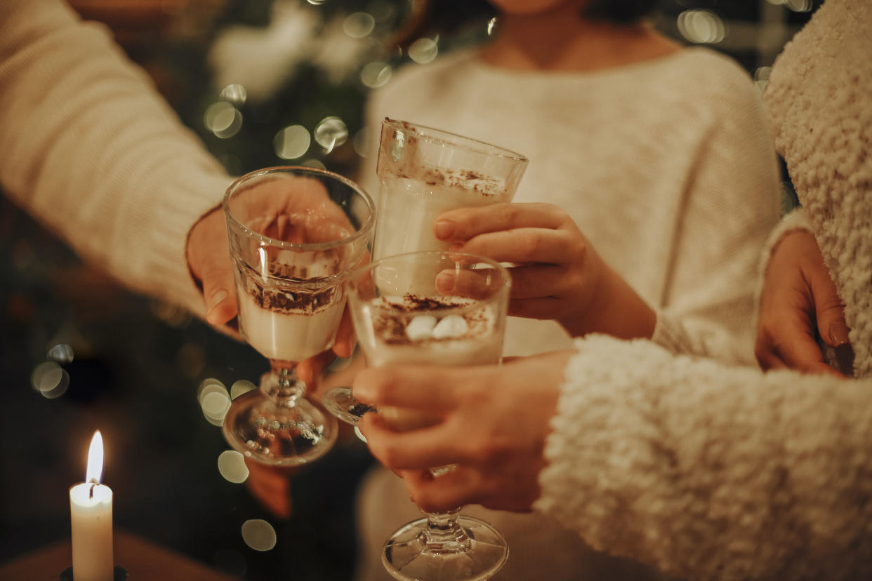 Family drinking homemade eggnog by the Christmas tree having fun. Beautiful woman and man with dauhter together. Christmas tree on background. Hygge concept