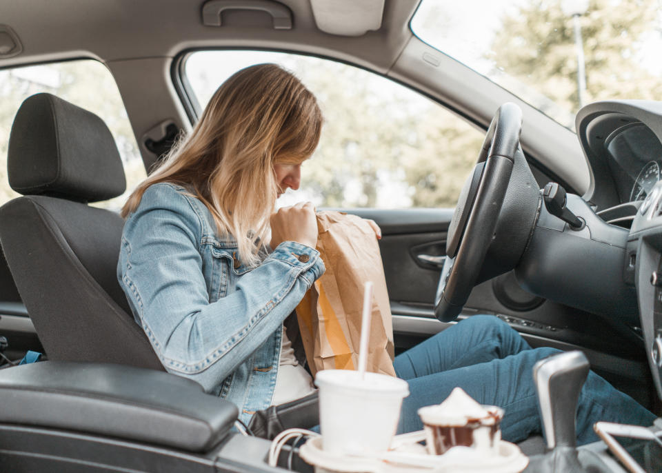 Young woman sitting in her car opens a McDonald's bag. 