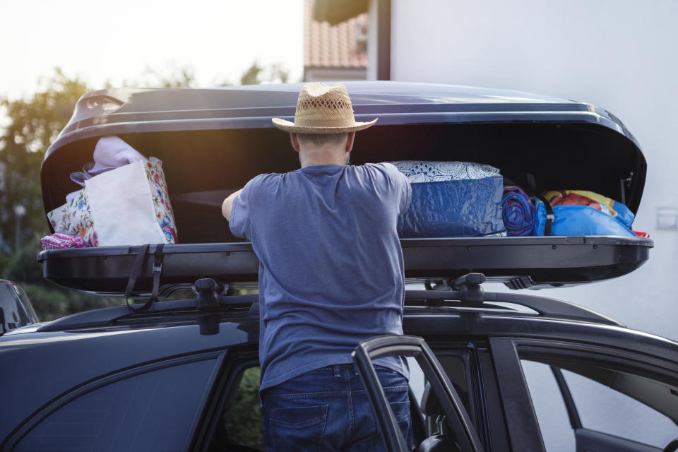 Man loading a car roof box with luggage before vacation