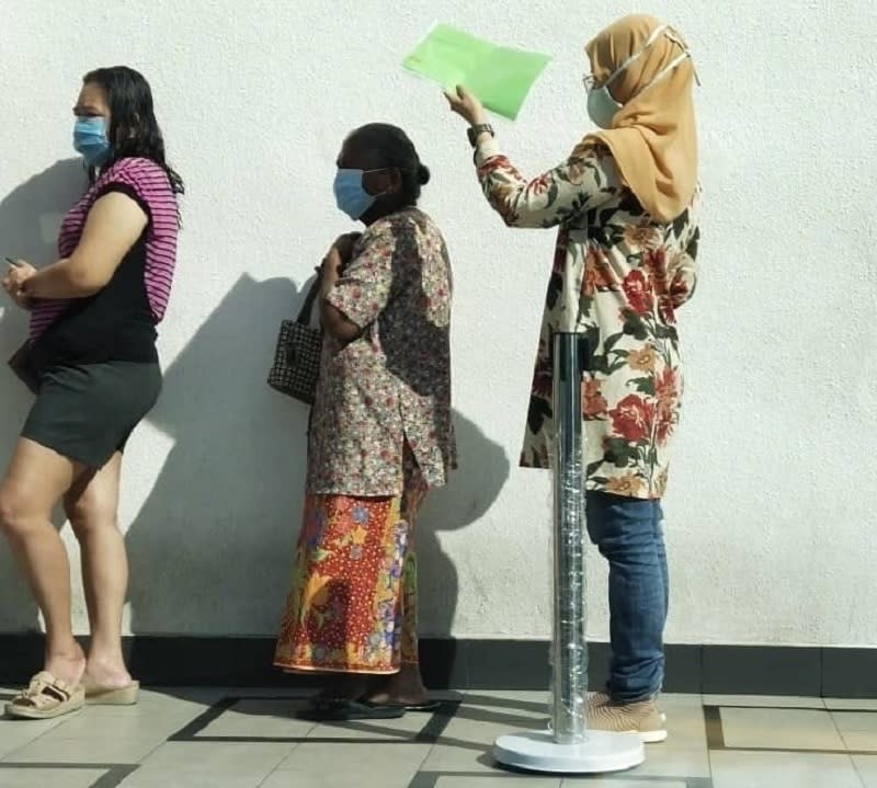 Hasrina Hassan holding a file to protect Lachumi Arunasalam from the hot weather that day. ― Picture via Facebook/PrivithaMaimaran