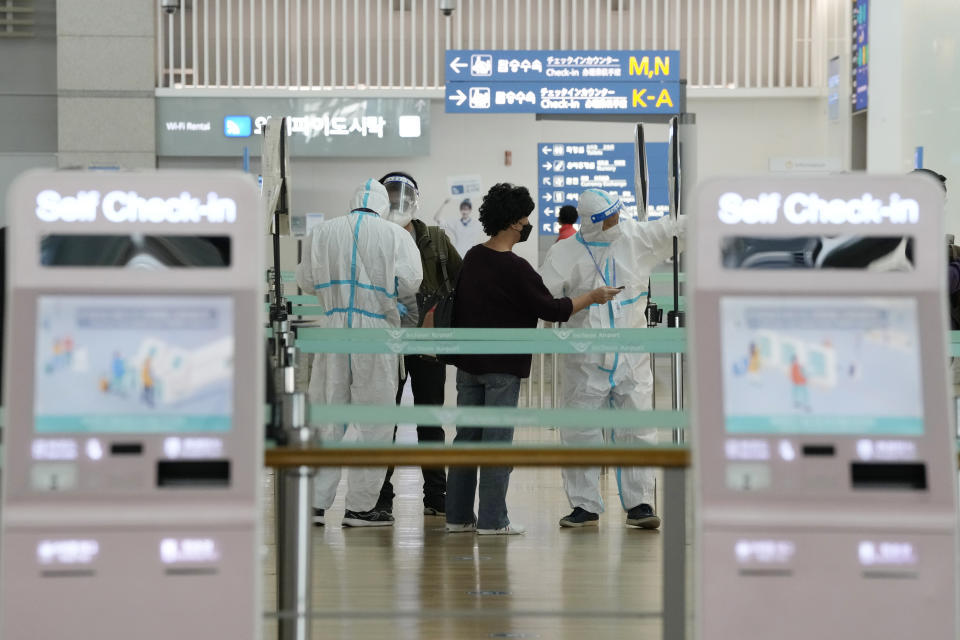 Staff members wearing protective gear guide passengers at the Incheon International Airport In Incheon, South Korea, Wednesday, Dec. 1, 2021. South Korea's daily jump in coronavirus infections exceeded 5,000 for the first time since the start of the pandemic, as a delta-driven surge also pushed hospitalizations and deaths to record highs. (AP Photo/Ahn Young-joon).