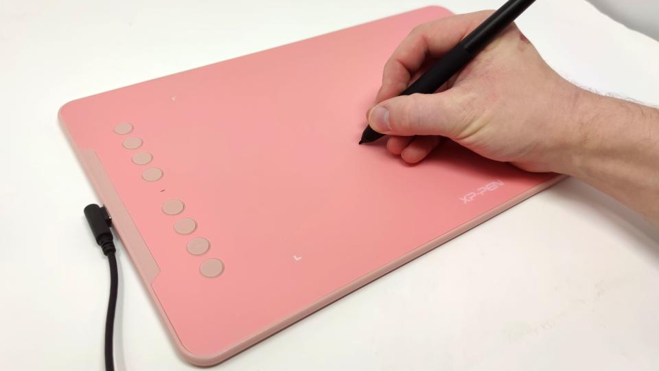 A hand holding a stylus drawing on the XP-Pen Deco 01 V2