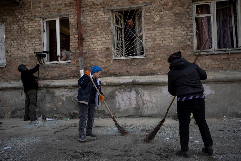 Residents clean up a street outside apartments damaged by shelling, in Kyiv, Ukraine, on March 23, 2022.