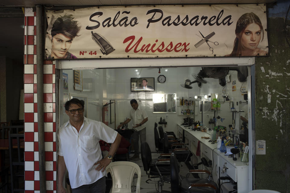 A hairdresser waits for customers at his shop in the the Rocinha slum of Rio de Janeiro, Brazil, Monday, March 16, 2020. Since the outbreak of the new coronavirus, nations have begun imposing travel restrictions and closing their borders to contain the pandemic's spread. The latest attempt to impose controls is a smaller territory: the hillside slum of Rocinha in Rio de Janeiro. (AP Photo/Silvia Izquierdo)