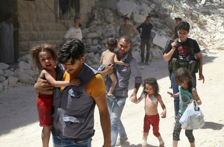 Syrian men carry injured children amid the rubble of destroyed buildings following air strikes in Aleppo on July 25, 2016
