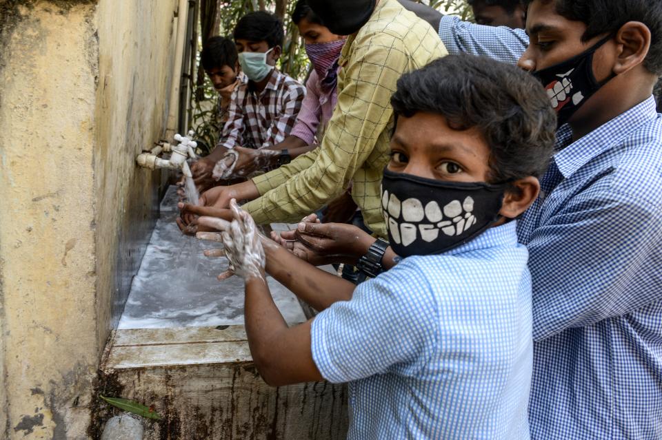 Students wearing facemasks wash their hands before attending a class at a governement-run high school in Secunderabad.