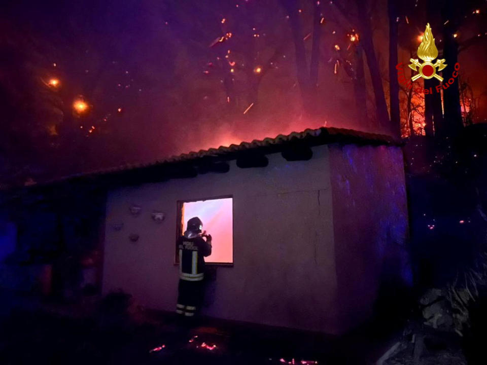 A firefighter checks a building as a wildfire burns near the Sicilian village of Curcuraci near Messina, Italy, July 25, 2023. Vigili del Fuoco/Handout via REUTERS ATTENTION EDITORS THIS IMAGE HAS BEEN SUPPLIED BY A THIRD PARTY. DO NOT OBSCURE LOGO.