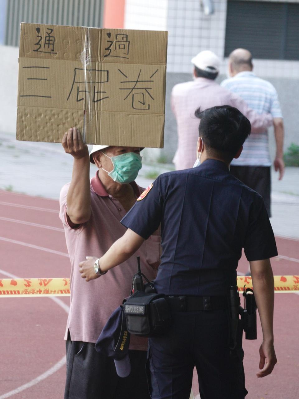 有人在投票所警戒線內高舉「通過三屁卷」，遭警方關切。   圖：張良一/攝