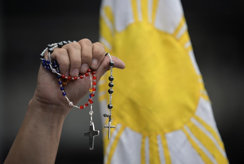 A Filipino wellwisher holds up rosaries in front of a Philippine flag while waiting for the motorcade of Pope Francis near the Apostolic Nunctiature in Manila