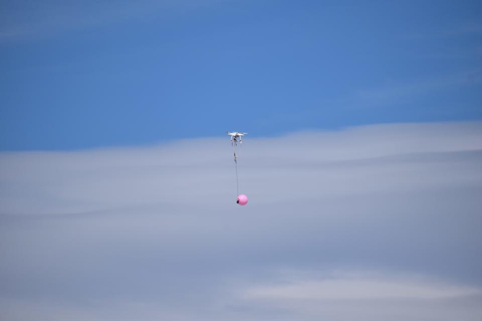 Operators shoot at a balloon dangling from a small drone.