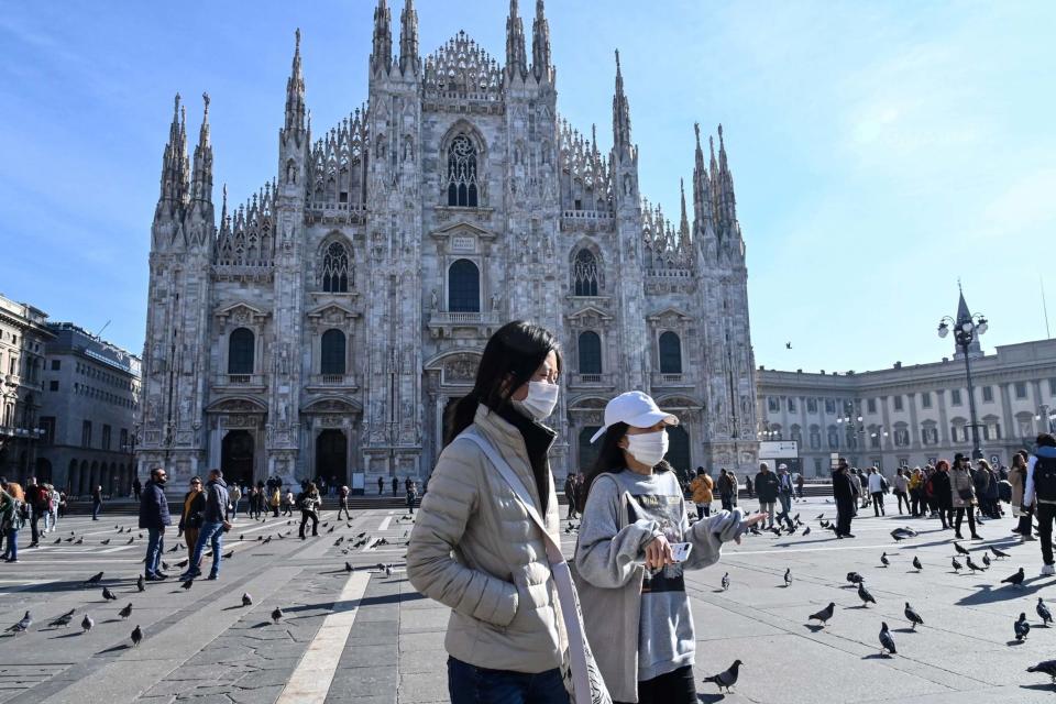 Two women wearing a protective facemask walk across the Piazza del Duomo in central Milan (AFP via Getty Images)