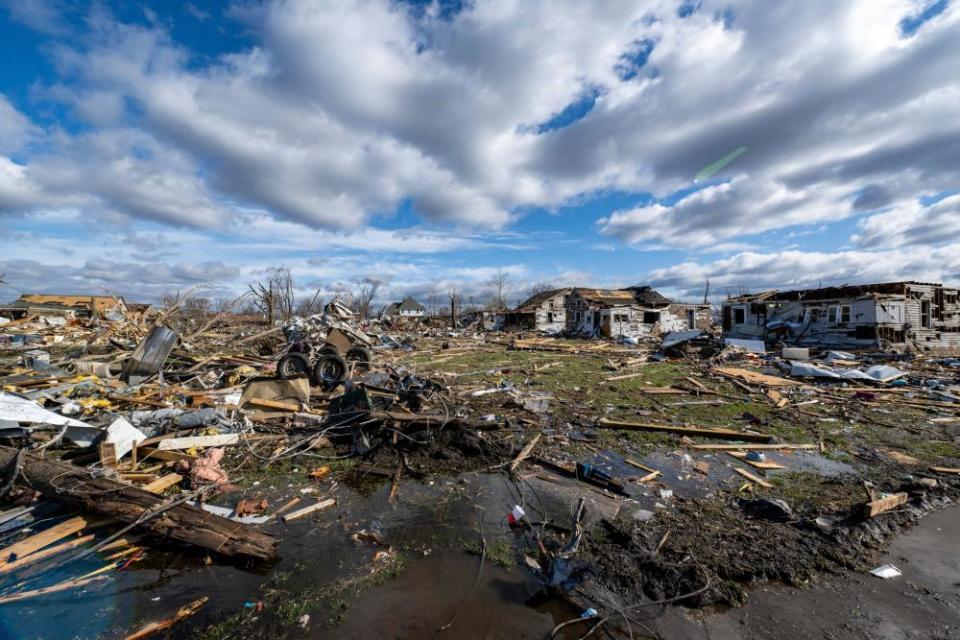 Debris from several homes destroyed by a tornado is strewn across a grassy area.