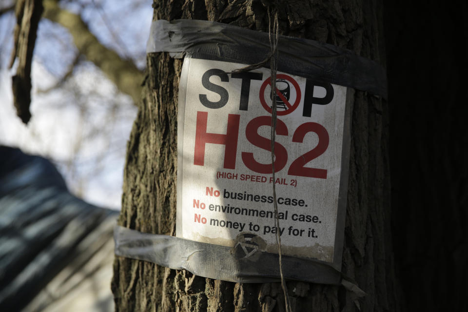 A protest sign is displayed on a tree by a roadside protest camp across the street from a High Speed 2 (HS2) rail line compound near the village of Harefield in north west London, Tuesday, Feb. 11, 2020. Britain's Conservative government is set to approve a contentious, expensive plan for a high-speed rail line linking London with central and northern England, despite opposition from environmentalists and even some members of the governing party. (AP Photo/Matt Dunham)