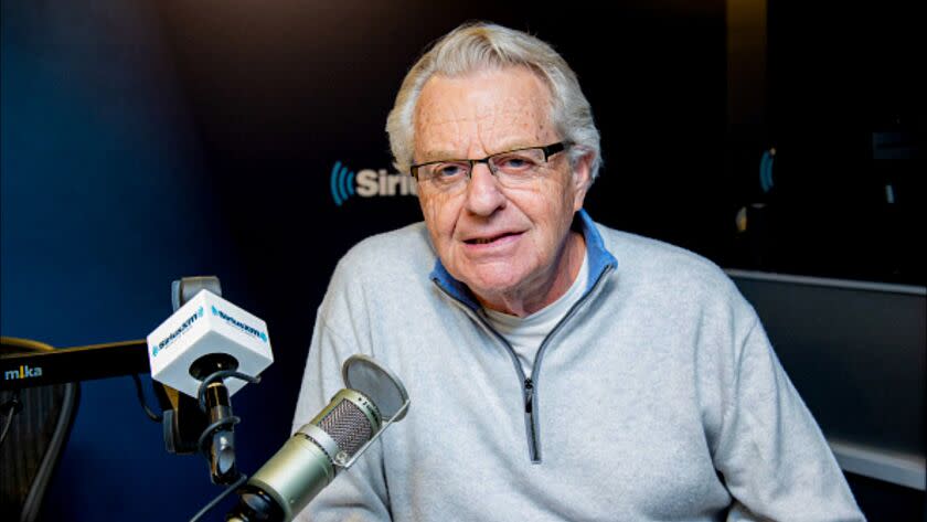 Jerry Springer dressed casually and seated behind several radio microphones