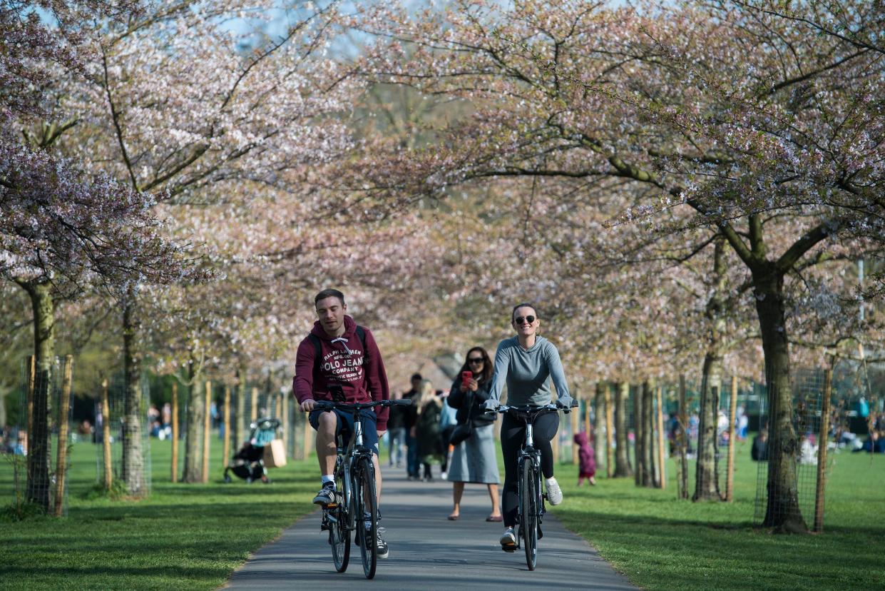 <p>People cycle under blossom in Battersea Park, London</p> (PA)