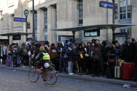 A woman rides her bicycle as commuters wait for a bus at Gare du Nord Station, in Paris, Tuesday, Dec. 10, 2019. Only about a fifth of French trains ran normally Tuesday, frustrating tourists finding empty train stations, and most Paris subways were at a halt. French airport workers, teachers and others joined nationwide strikes Tuesday as unions cranked up pressure on the government to scrap changes to the national retirement system. (AP Photo/Francois Mori)