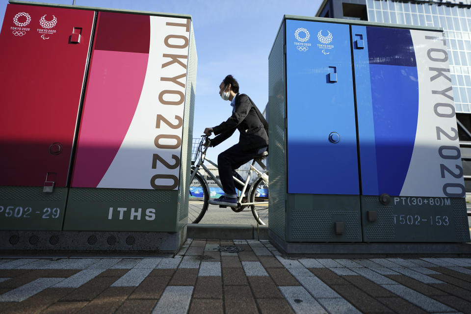 A man wearing a protective face mask rides a bicycle past some Tokyo 2020 Olympic and Paralympic Games advertisements Monday, April 12, 2021, in Tokyo. (AP Photo/Eugene Hoshiko)