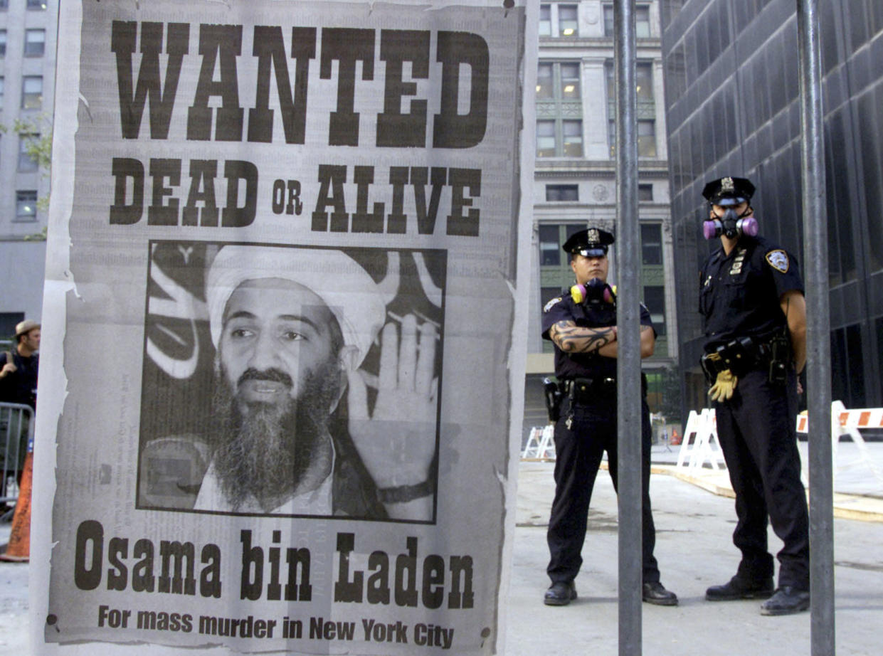 Two police officers stand near a wanted poster after the 9/11 attacks. The poster reads: Wanted dead or alive, Osama bin Laden, for mass murder in New York City.