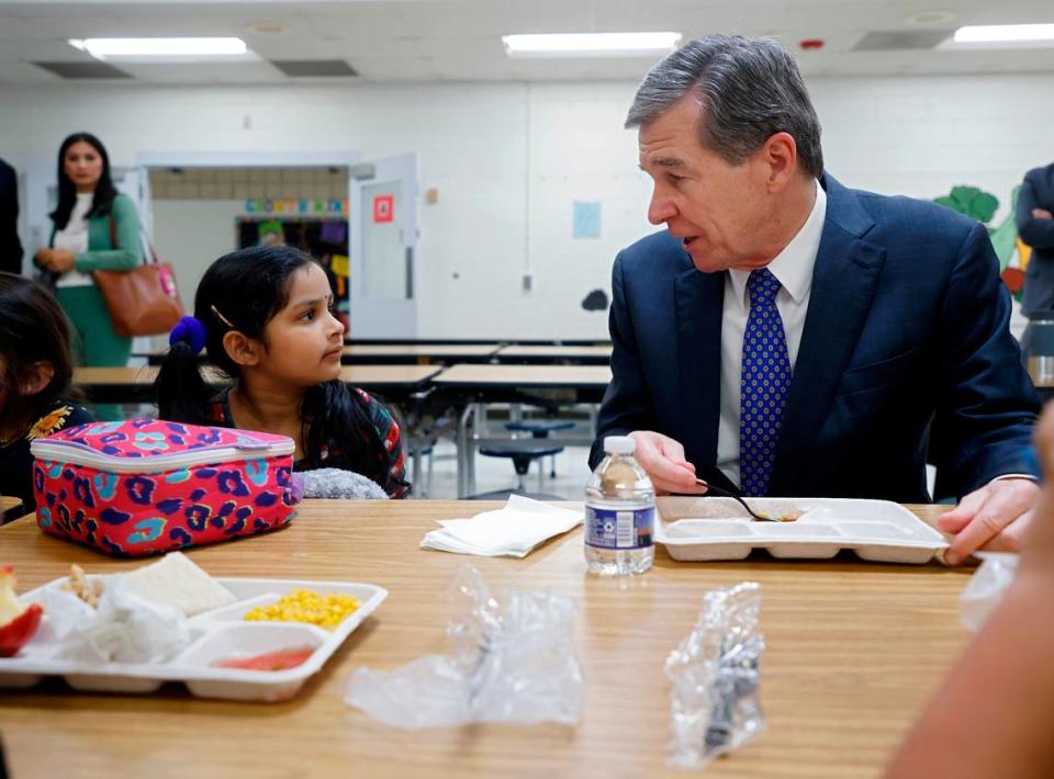 Gov. Roy Cooper speaks with kindergarten student Sankeerthana Lolla while eating lunch at Bethesda Elementary School on Tuesday, Oct. 11, 2022, in Durham, N.C. Cooper visited the school to announce new agreements to bring food from North Carolina farmers and producers to schools.