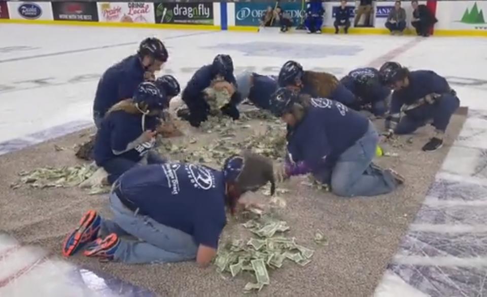 Maestros compitieron para agarrar la mayor cantidad de los 5,000 billetes de un dólar donados en un evento durante un partido de hockey sobre hielo en Dakota del Sur. (Twitter/@AnnieTodd96)