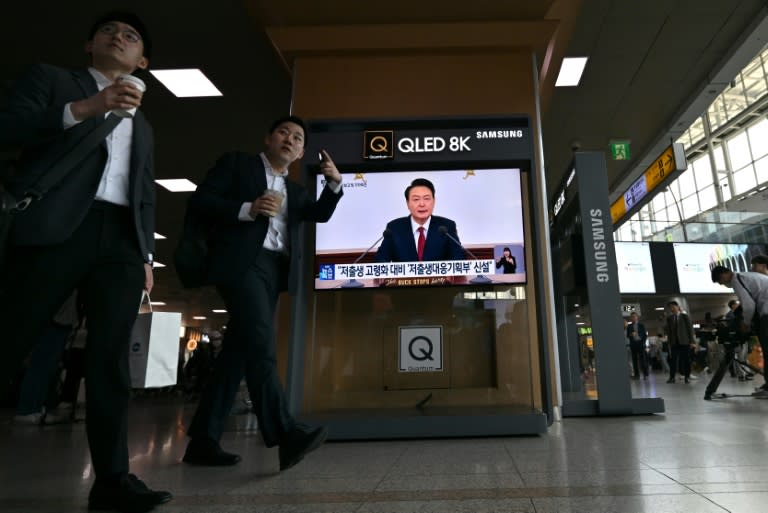 People at a Seoul railway station walk past a screen carrying live footage of South Korean President Yoon Suk Yeol's Thursday press conference (Jung Yeon-je)