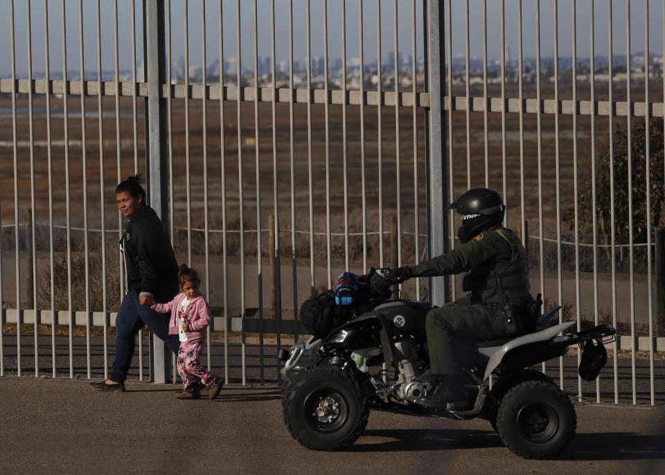 La migrante hondureña Rachel Rivera, de 19 años, y su hija Charlot Andrea, de 3 años, caminan a lo largo de una cerca fronteriza en San Ysidro, California, luego de entregarse a los agentes de la Patrulla Fronteriza de Estados Unidos, el jueves 4 de diciembre de 2018. (AP Foto/Rebecca Blackwell)