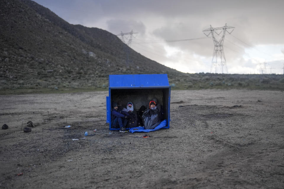 Asylum-seeking migrants from Peru and Ecuador take shelter from the wind and rain as they wait to be processed in a makeshift, mountainous campsite after crossing the border with Mexico, Friday, Feb. 2, 2024, near Jacumba Hot Springs, Calif. (AP Photo/Gregory Bull)