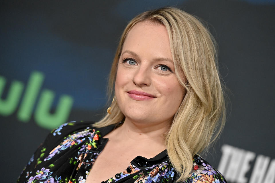 Elisabeth Moss is smiling at a red carpet event, wearing a floral dress