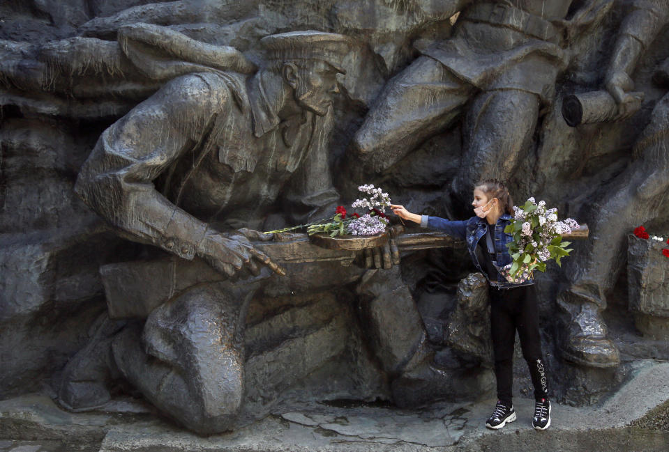 A girl wearing a face mask to protect against coronavirus lays flowers to the monument of the Unknown Soldier at a memorial to World War II veterans in a memorial park in Kyiv, Ukraine, Saturday, May 9, 2020 on the 75th anniversary of the end of World War II. Ukraine marks the 75th anniversary of the end of World War II in Europe at a time of coronavirus lockdown and loneliness spent in search of memories both bitter and sweet. (AP Photo/Efrem Lukatsky)