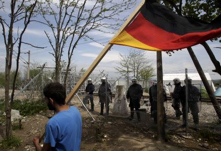A migrant carries a German flag in front of Greek police at a makeshift camp at the Greek-Macedonian border near the village of Idomeni, Greece, April 11, 2016. REUTERS/Alexandros Avramidis