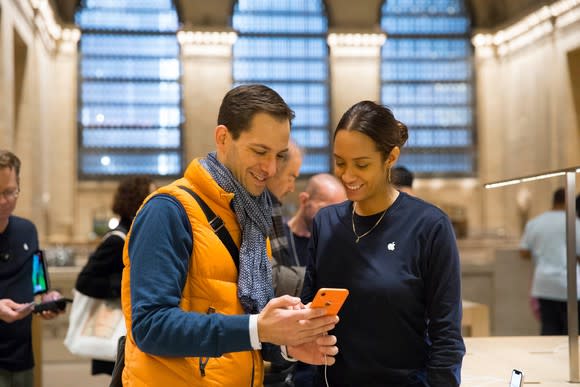 A man holding an orange iPhone XR with an Apple employee next to him.