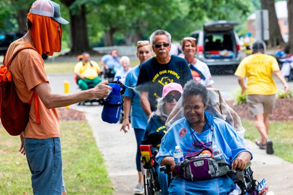 Joe Tate, a personal care assistant, mists Karen Burrison, among demonstrators rallying outside the North Carolina Department of Health and Human Services on Monday, June 24, 2024. About 50 demonstrators with National ADAPT rallied outside the office to mark the 25th Anniversary Rally of the Olmstead Decision in North Carolina.