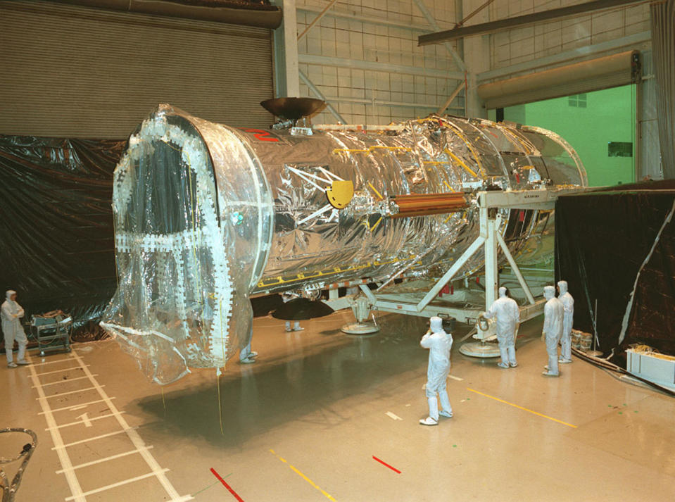 Scientists in cleanroom suits work on the Hubble Space Telescope inside a large indoor facility