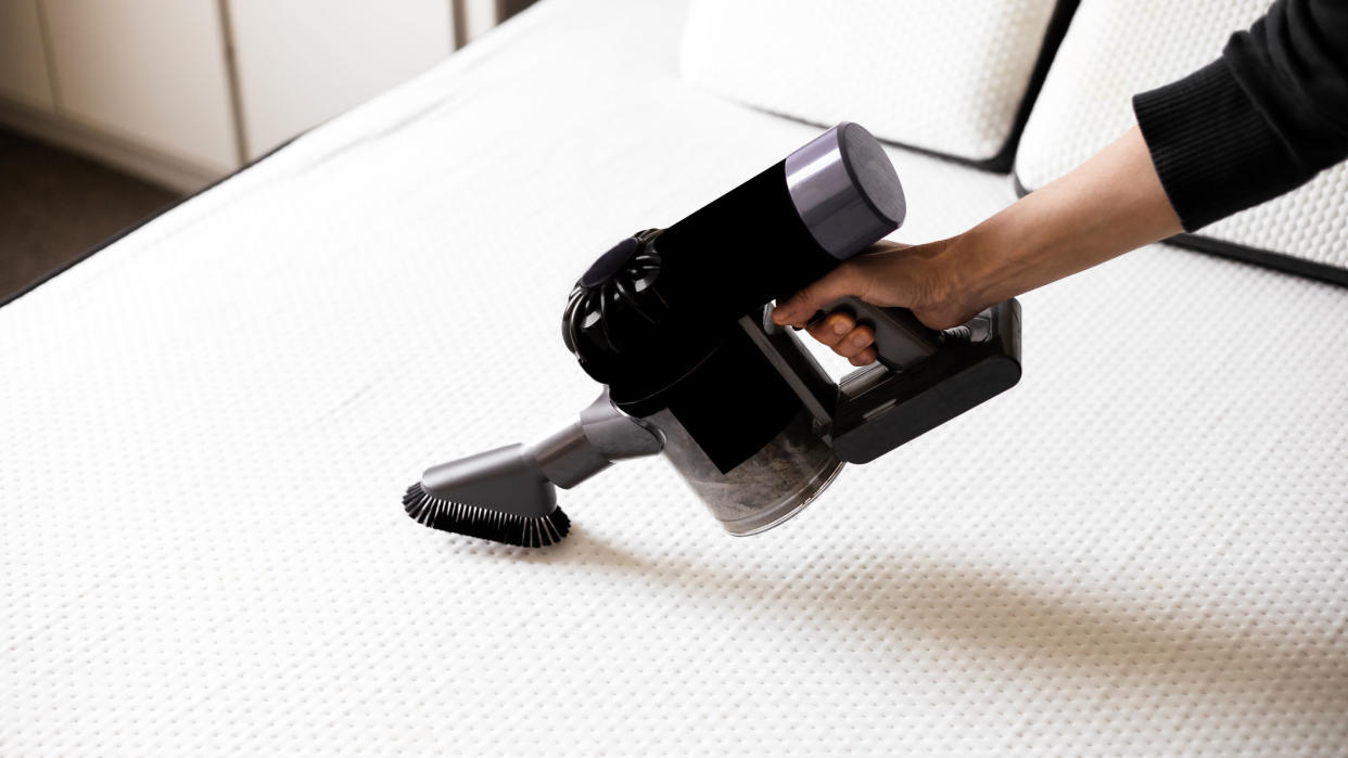  Image shows a person vacuuming a white mattress before cleaning mold off of it. 